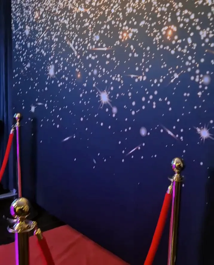 Crveni tepih i zlatni stupići s užetom ispred zvjezdane pozadine photobootha