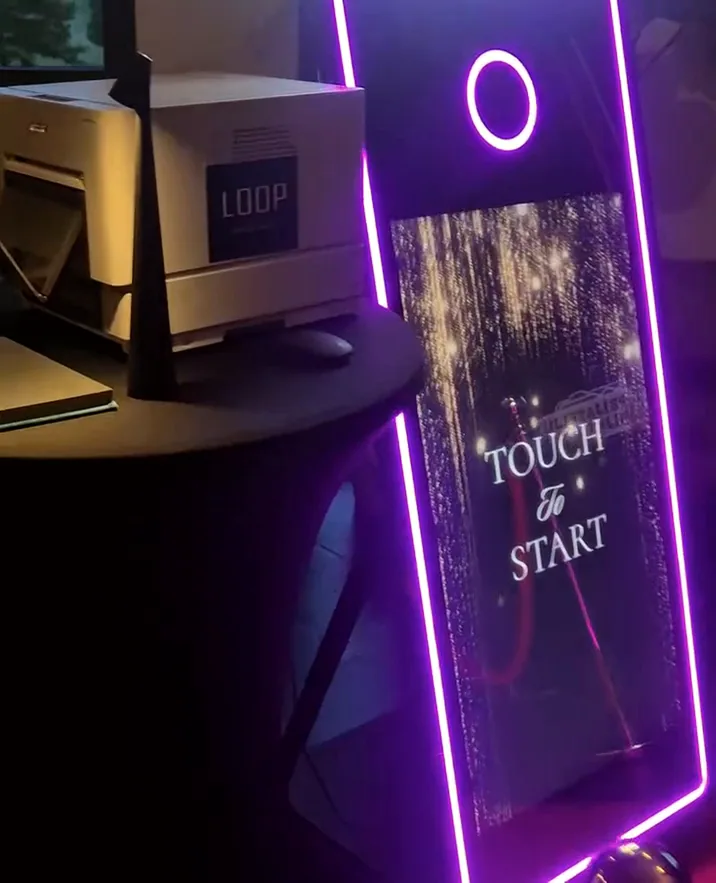 Mirror photobooth s ljubičastim neonskim rubom i natpisom Touch to start, uz LOOP printer