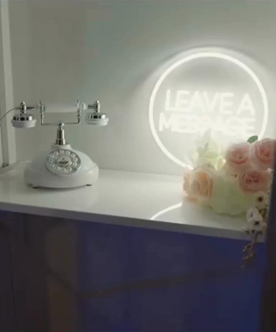 Bijeli starinski telefon za audio poruke gostiju ispod svjetlećeg natpisa Leave a message